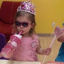 A young child wearing a tiara and sunglasses holds a sippy cup and a toy wand.