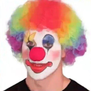 Clown with a rainbow wig and white face paint smiling at the camera.