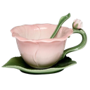 A pink flower-shaped teacup with a green stem handle and a matching spoon resting on a leaf-shaped saucer.