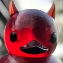 A glossy red duck with small devil horns looking directly at the camera with a mischievous expression.