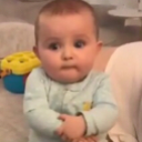 A baby with a serious, skeptical expression looking directly at the camera.