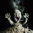 Baby covered in dust screaming with mouth wide open while emerging from a pile of dirt.