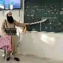 A man with a long black beard and traditional clothing points a large sword at a green chalkboard.