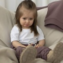 A toddler sitting on a couch with a skeptical and unimpressed facial expression.