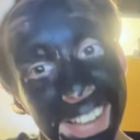Person with a black charcoal face mask smiling widely at the camera.