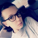 Millie Bobby Brown wearing glasses looking at the camera with a skeptical and unimpressed expression.