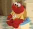 Elmo from Sesame Street wiggles and dances while sitting on a small potty.