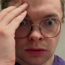 Man with glasses holding his forehead in a gesture of disbelief and shock.