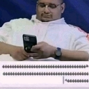 A man wearing glasses looks down at his smartphone with a serious, focused expression.