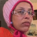 Doja Cat wearing a pink beanie and glasses looking directly at the camera with a skeptical and confused facial expression.