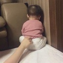 Baby sitting in a corner facing the wall while a hand reaches out to touch their back.