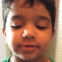 A young child with dark hair and a green shirt has their eyes closed in a serious expression.