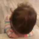 A baby with brown hair resting their head on their hands while wearing a striped shirt.