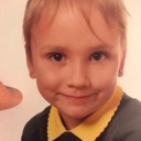 Child with blonde hair and a yellow collar giving a smug, knowing smirk.