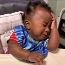 Baby crying with their hand held against their forehead in a dramatic gesture of frustration.