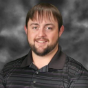 A man with a beard and a polo shirt smiling gently at the camera.