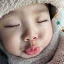 A baby with eyes closed and lips puckered in a kiss gesture while wearing a fuzzy winter hat.