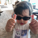 Toddler wearing dark sunglasses gives a double thumbs-up gesture.