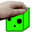 A human hand gently pats a small green square slime on the head.