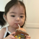 A toddler with a blank expression drinks from a juice box through a straw.
