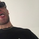 Man wearing sunglasses and a metal grill looking down at the camera.