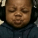 A young boy with eyes closed and lips pursed wearing black headphones.