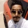 Man wearing dark sunglasses looking cool with an orange car in the background.