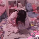 A girl sits on the floor in a pink room surrounded by plush toys while engaged in a quiet activity.