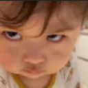 A toddler with a suspicious, side-eye expression and the word Achaa written over their face.