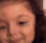 Baby with curly hair and a small heart filter on their cheek wearing a smug, knowing smirk.