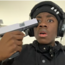 A young man wearing headphones looks at the camera with a shocked expression while holding a silver gun to his head.