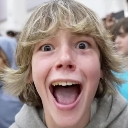 A young person with blonde hair looking directly at the camera with wide eyes and an open mouth in a state of shock.