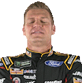 NASCAR driver in a black and gold racing suit performing a slow-motion facepalm.