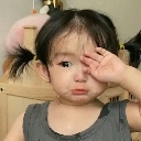 Toddler with pigtails wiping a tear from their eye with a pouty, sad facial expression.